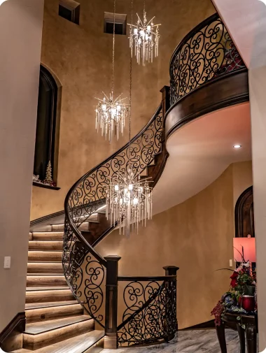Interior Makeovers Collections 5 Winding staircase with decorative metal scrollwork and three ornate chandelier.